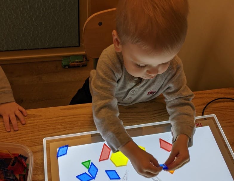 Child playing with colorful geometric shapes on a light table