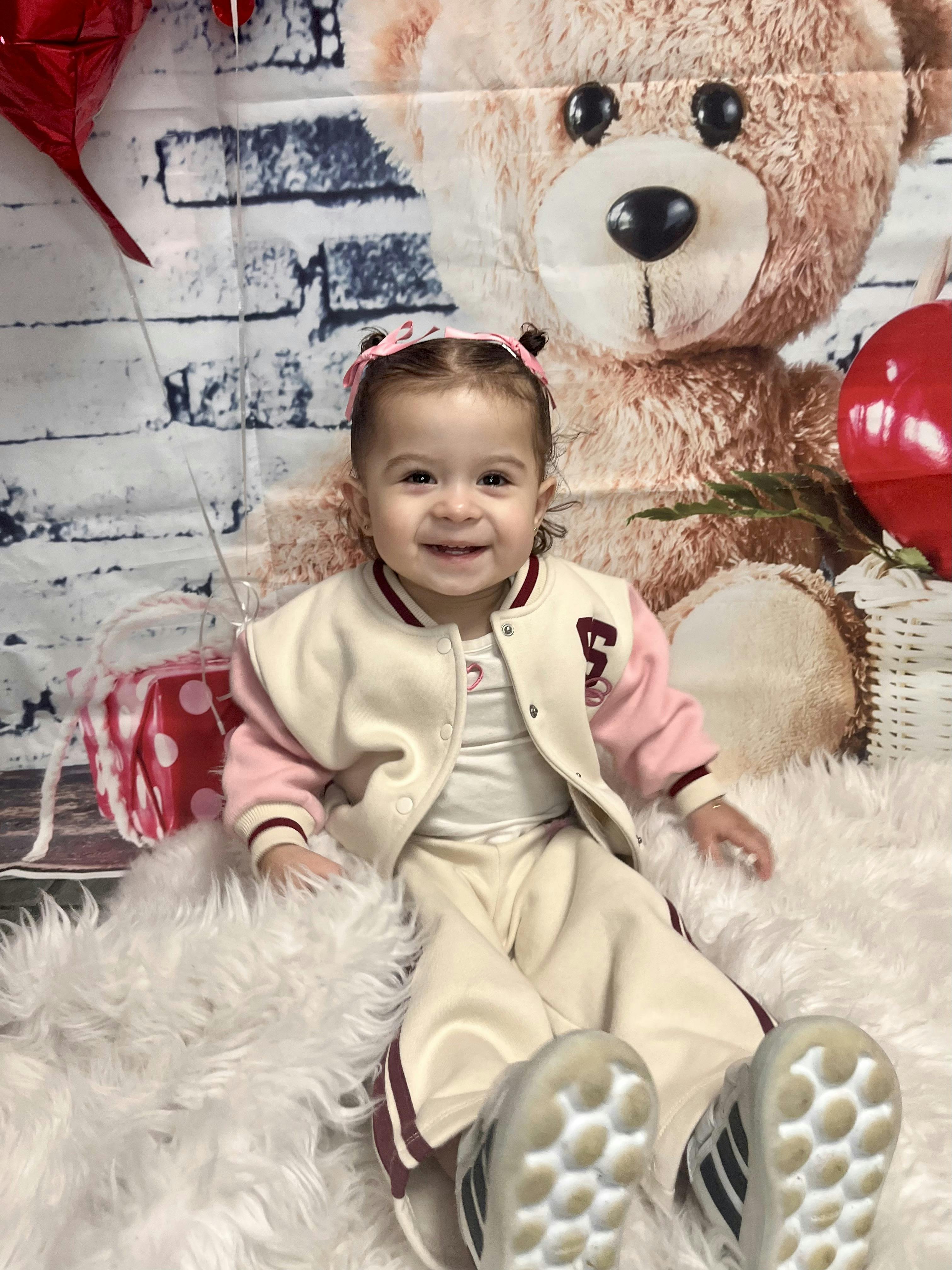 Child sitting on a white fluffy rug in front of a teddy bear backdrop