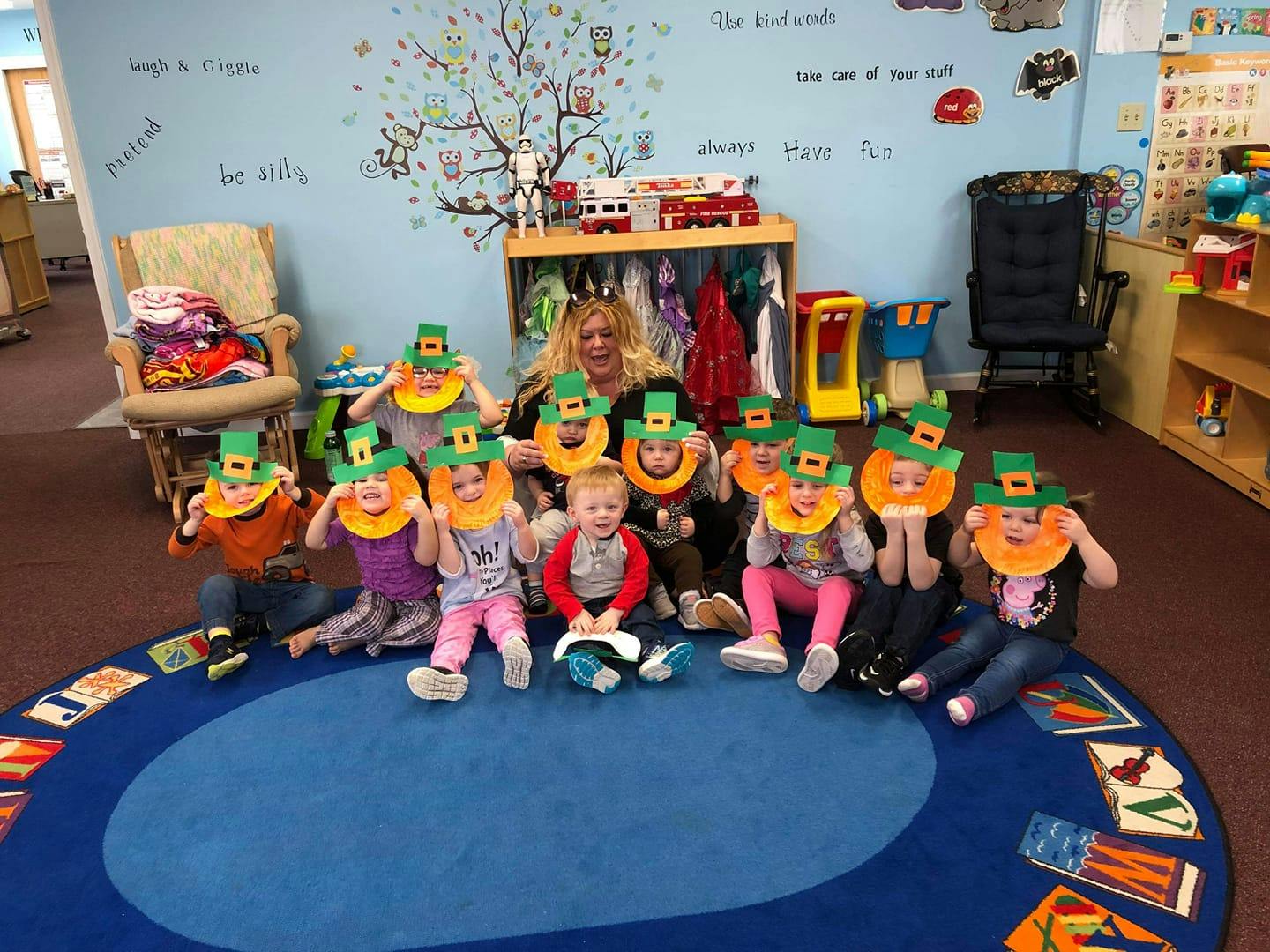 Adult and children wearing green hats and orange collars in a classroom