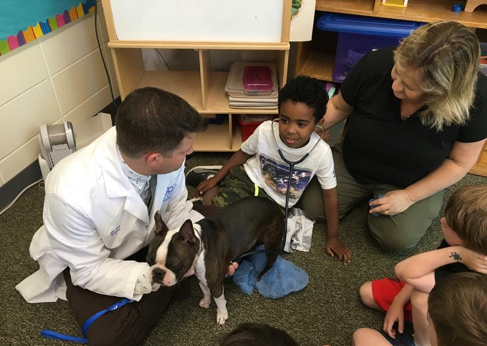 Person in lab coat holding a dog, child with stethoscope, and other people