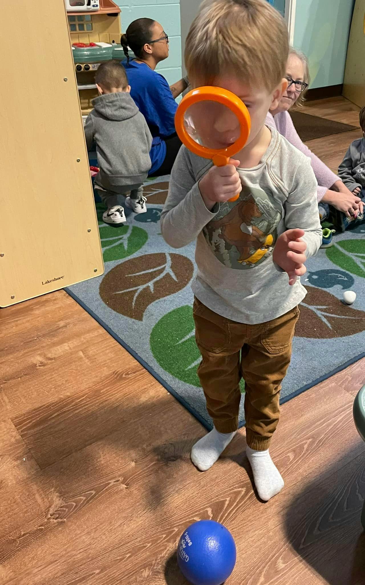 Child holding a magnifying glass to their face in a classroom