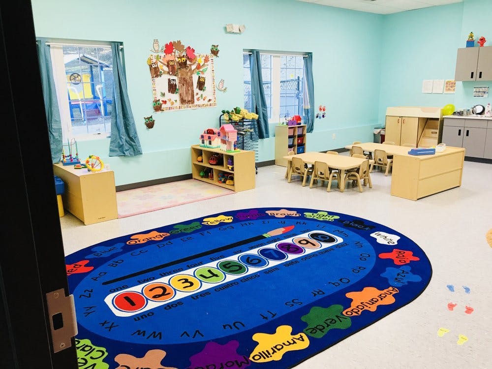 Classroom with small tables and chairs, shelves, and a colorful rug