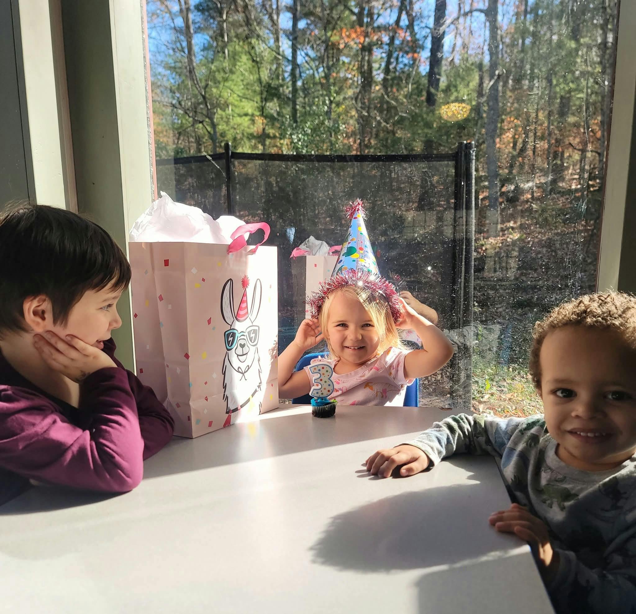 Three children at a table with a gift bag and a child wearing a party hat