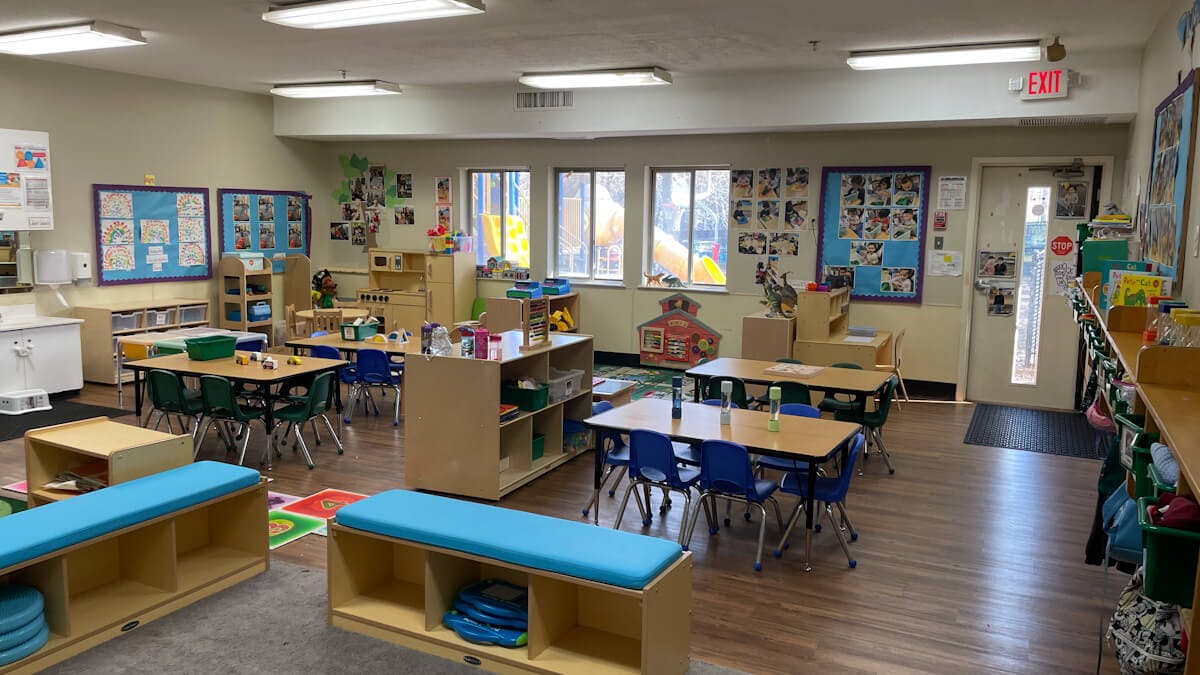 Classroom with small tables and chairs, shelves, and windows looking out to a playground