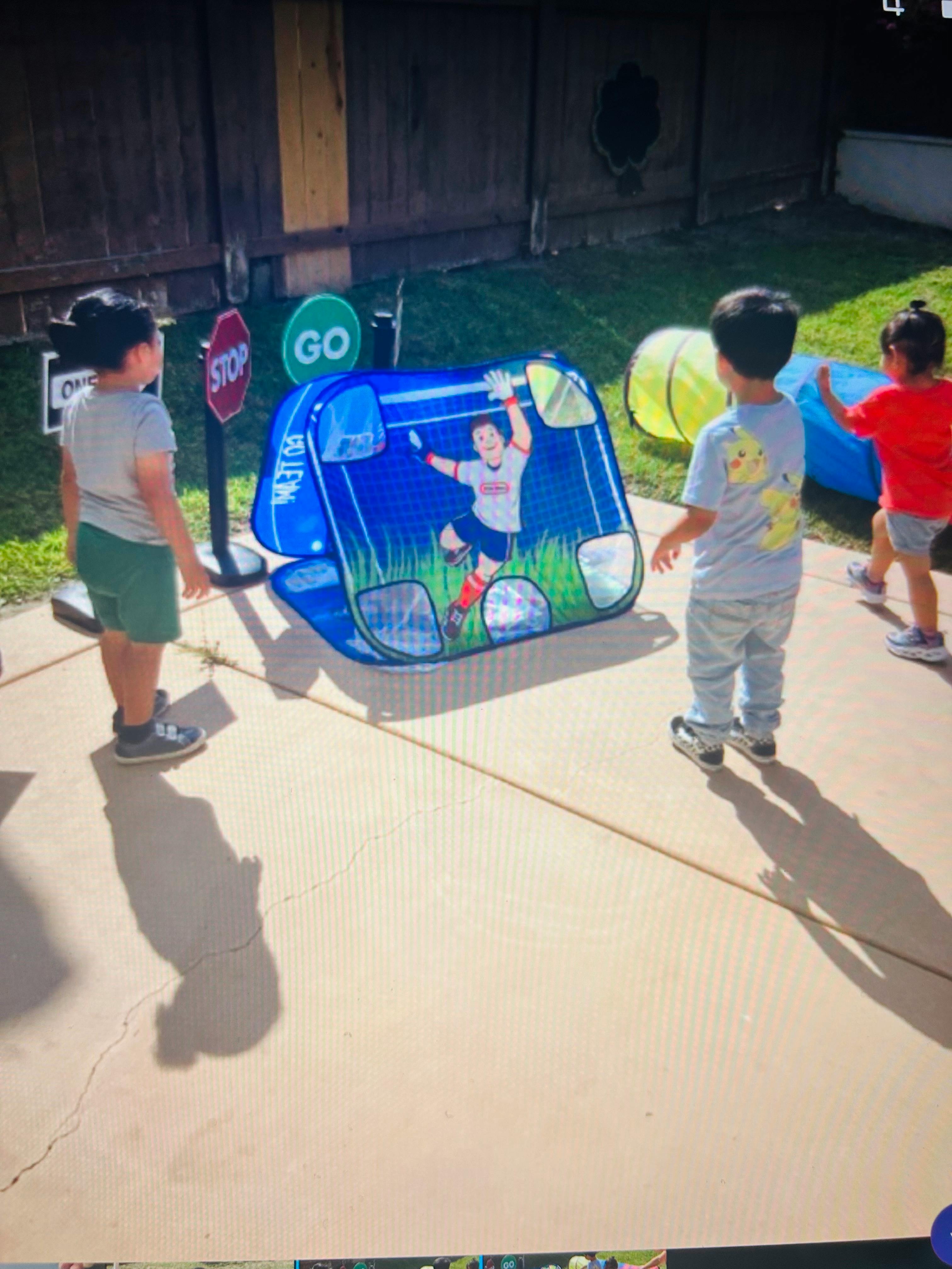 Three children playing outdoors with a blue pop-up soccer goal