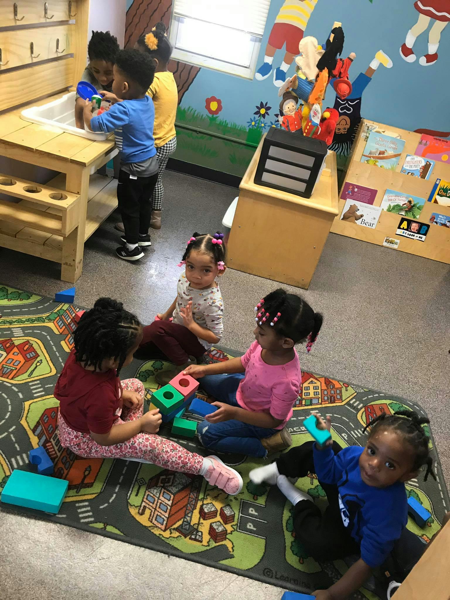 Children playing with blocks and at a water table in a classroom