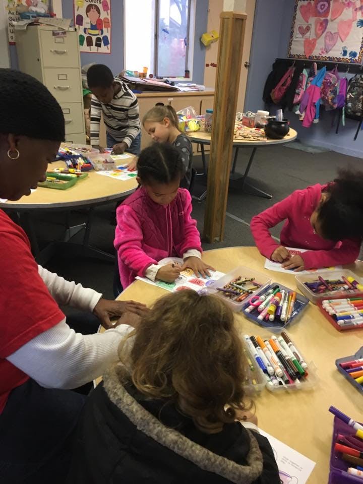 Adult and children drawing and coloring at tables in a classroom