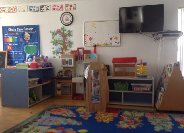 Classroom with a blue rug, shelves, and a wall-mounted TV