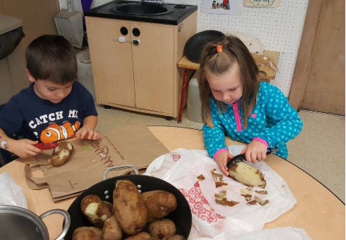 Two children peeling potatoes in a kitchen