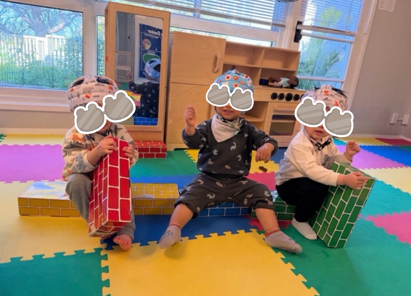 Three children playing with brick-patterned blocks in a room