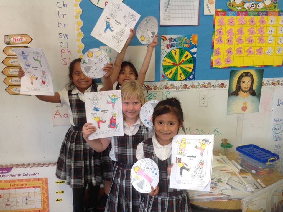Children in uniform holding up drawings in a classroom