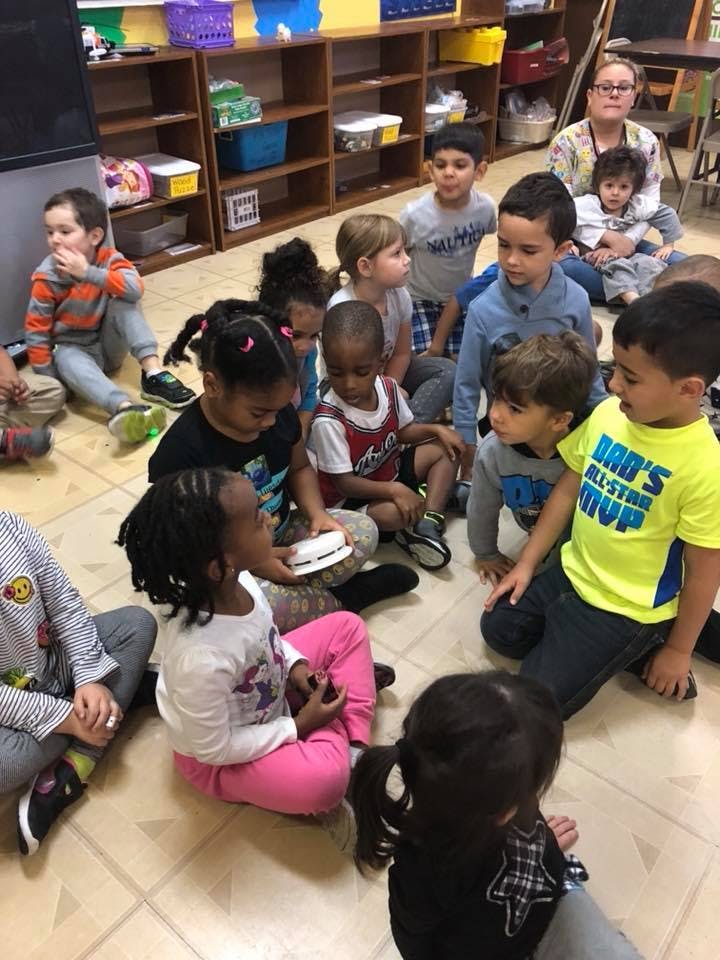 Group of children and one adult sitting on the floor in a classroom