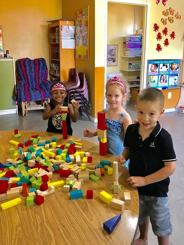 Three children playing with building blocks at a table in a classroom