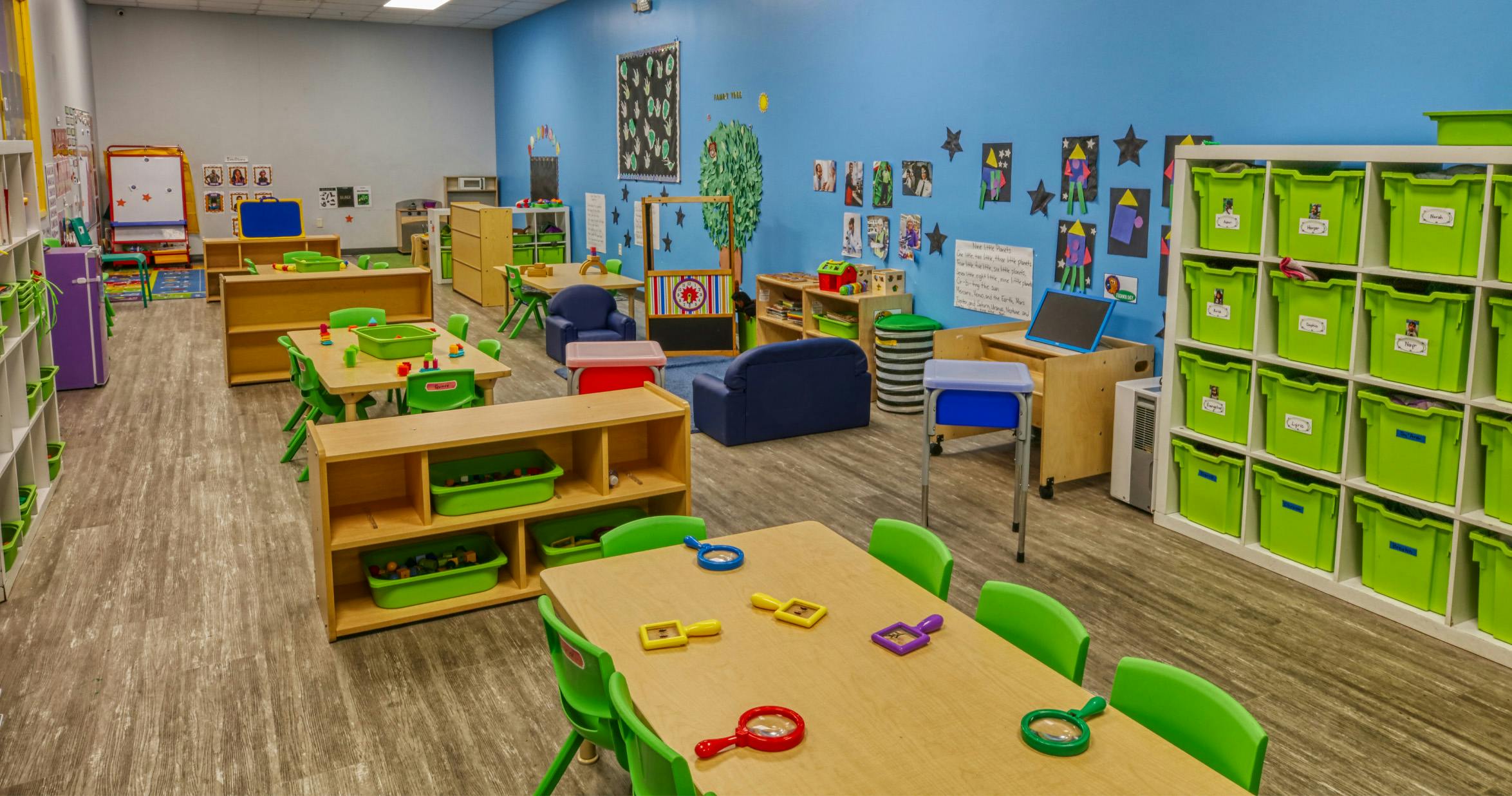 Classroom with child-sized tables and chairs, shelves, and a blue wall decorated with art