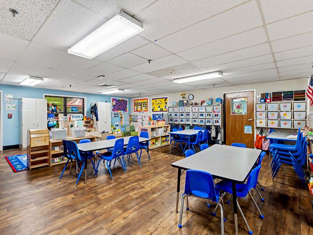 Empty classroom with small tables and chairs, white cabinets, and colorful decorations