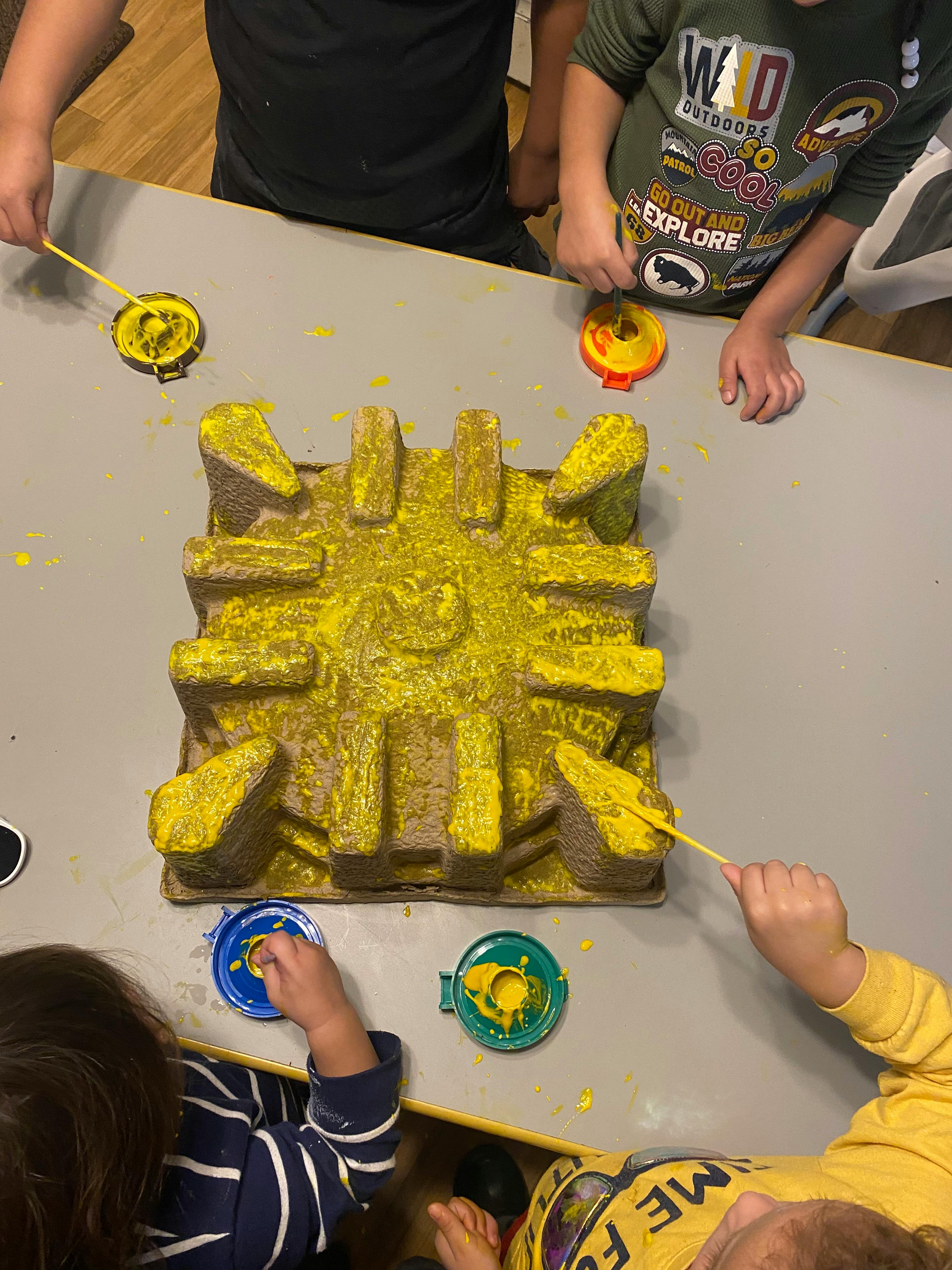 Children painting a cardboard structure yellow