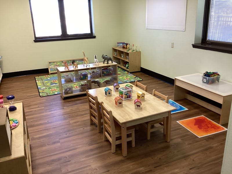 Playroom with small tables and chairs, shelves with toys, and rugs