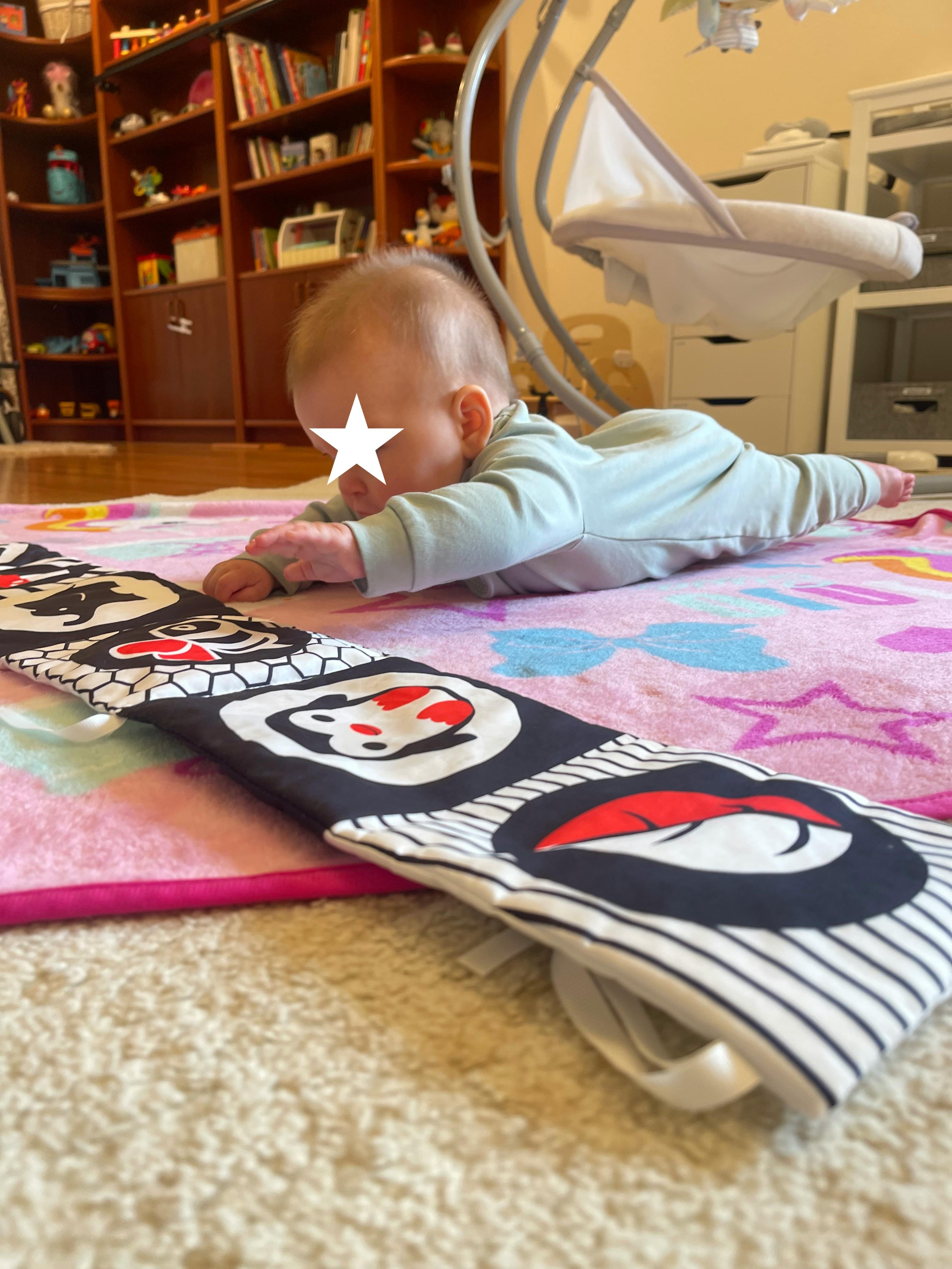 Child on stomach on a playmat looking at a soft book