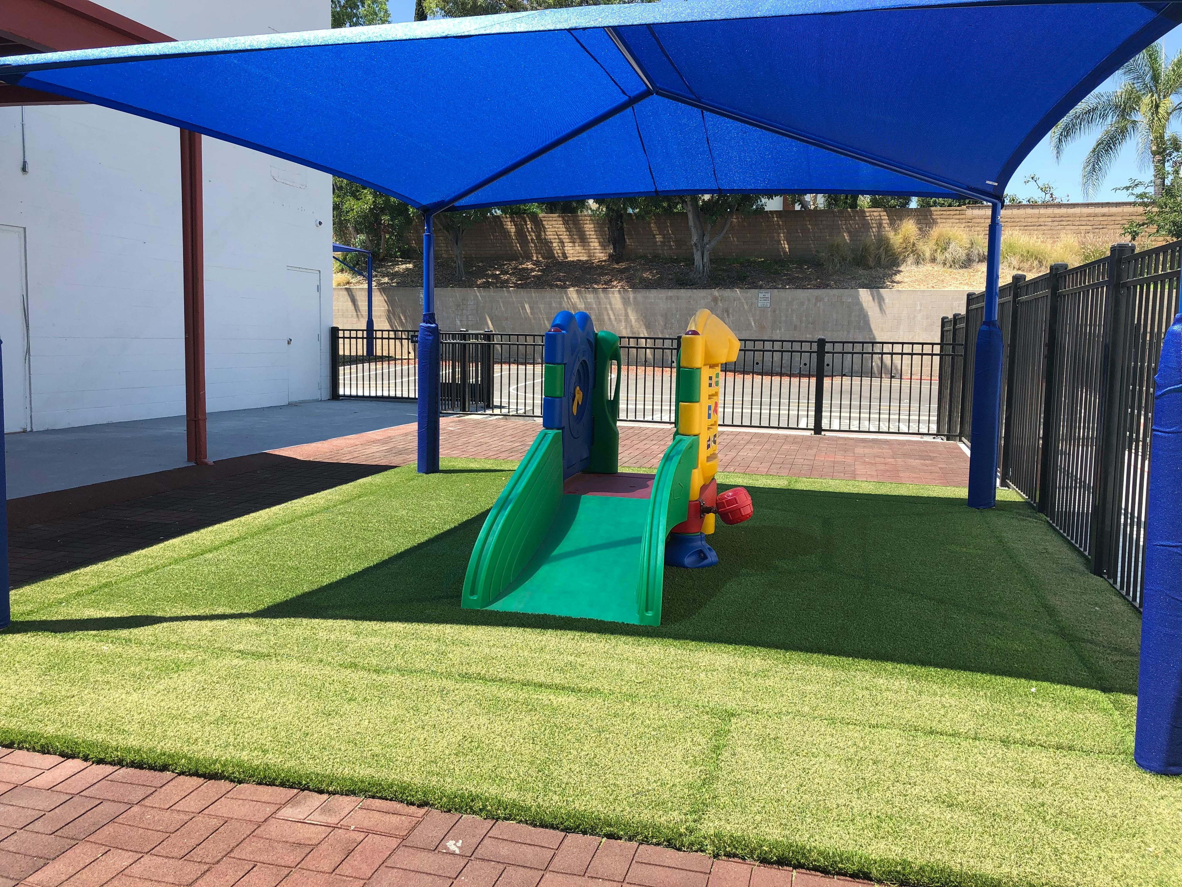 Playground with a blue shade structure over artificial turf and play equipment