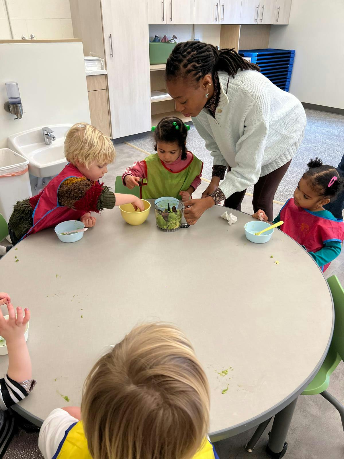 Adult and children preparing food together at a round table in a classroom