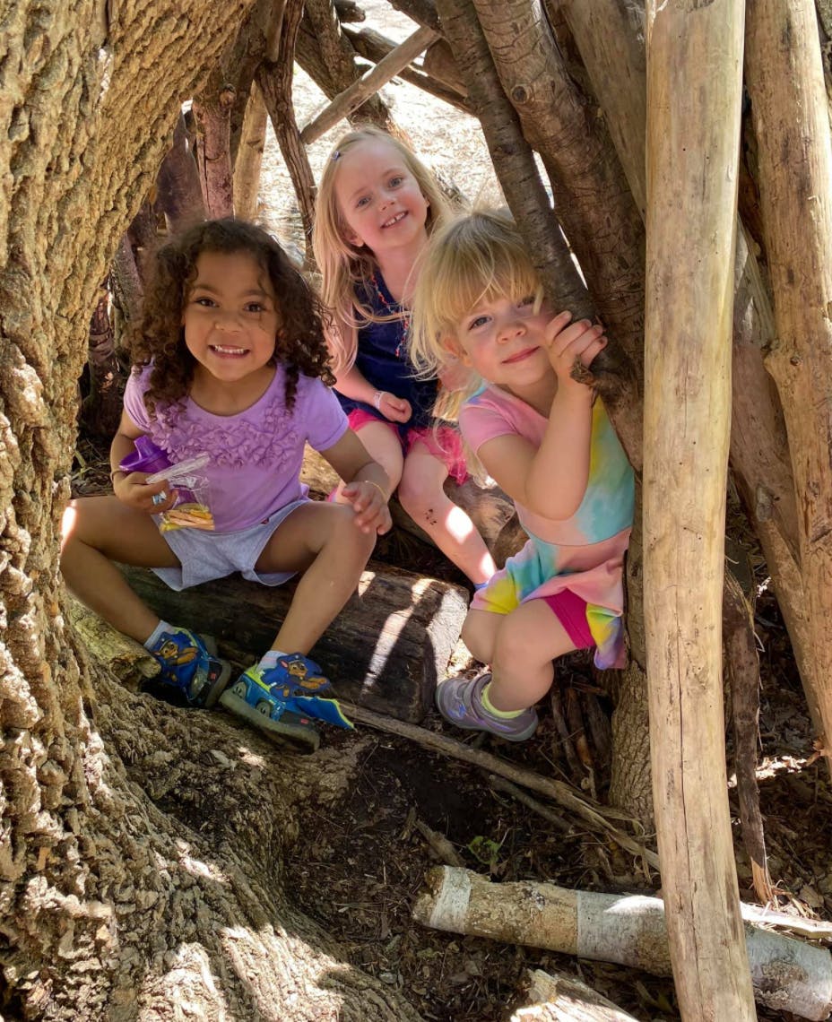 Three children sitting inside a stick fort