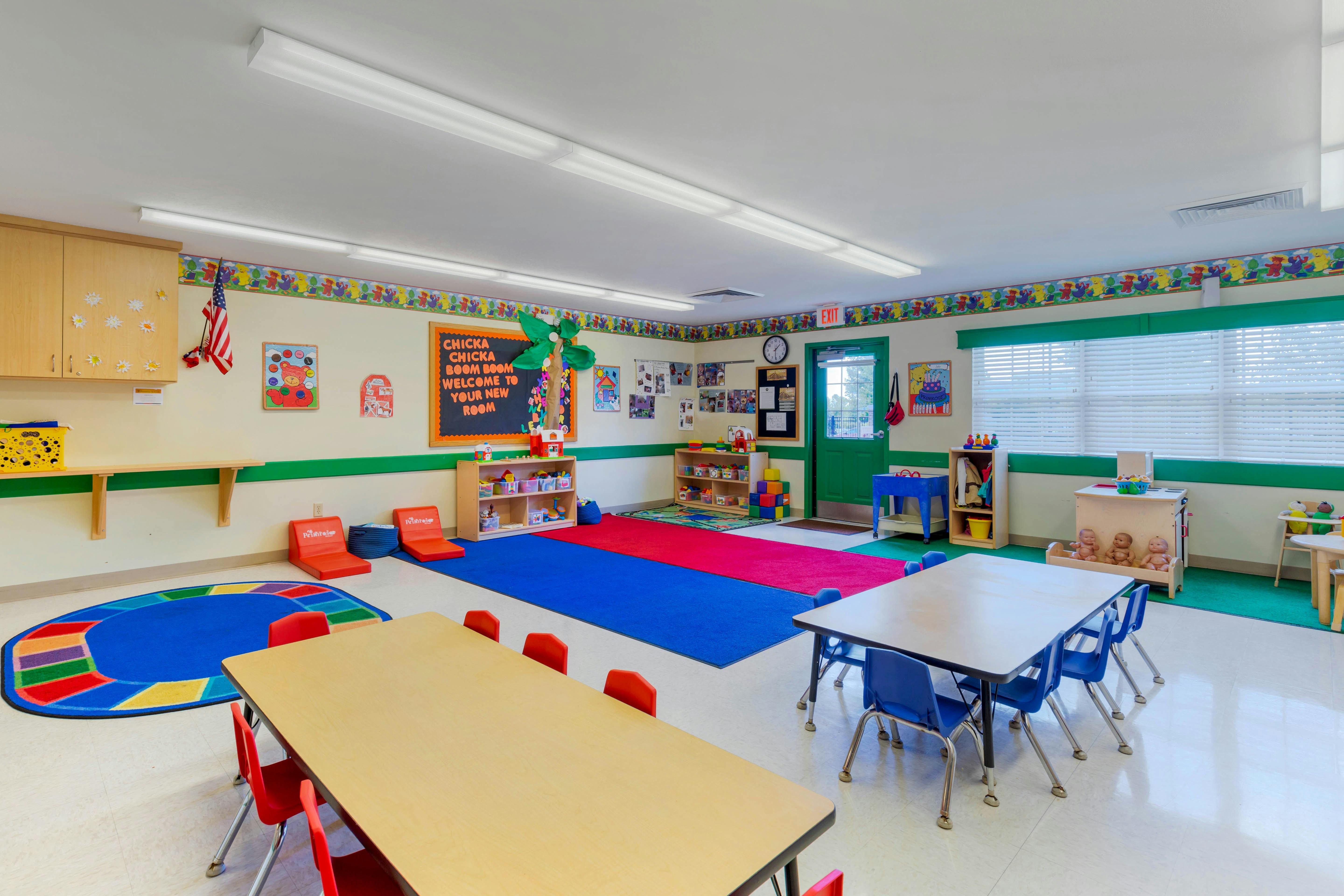 A colorful classroom with small tables and chairs for children, play mats, and toys