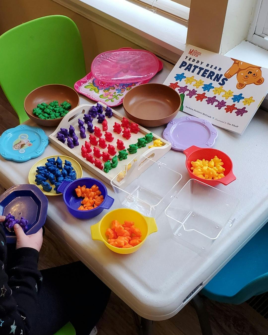 Child playing with colorful teddy bear counters and a patterns book