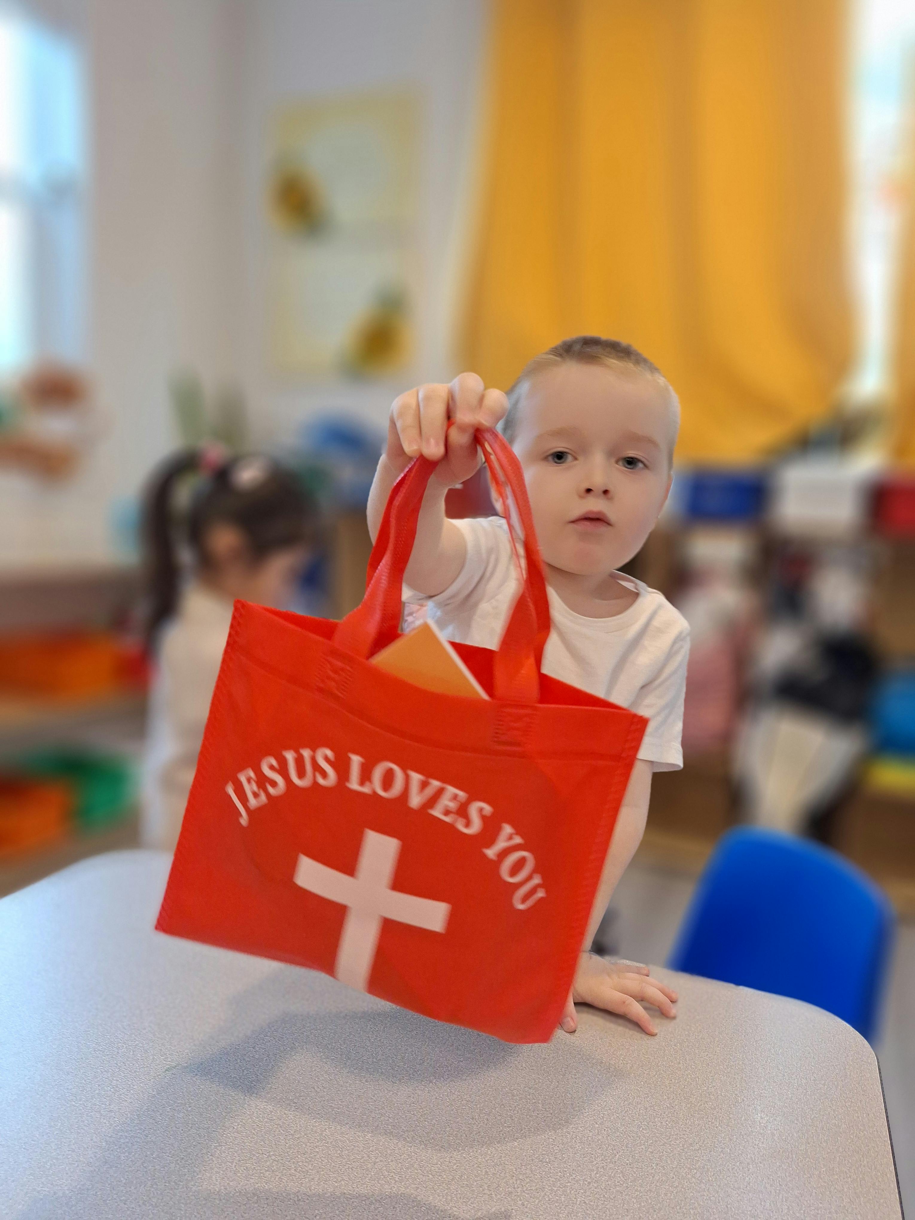 Child holding a red bag that says "JESUS LOVES YOU"