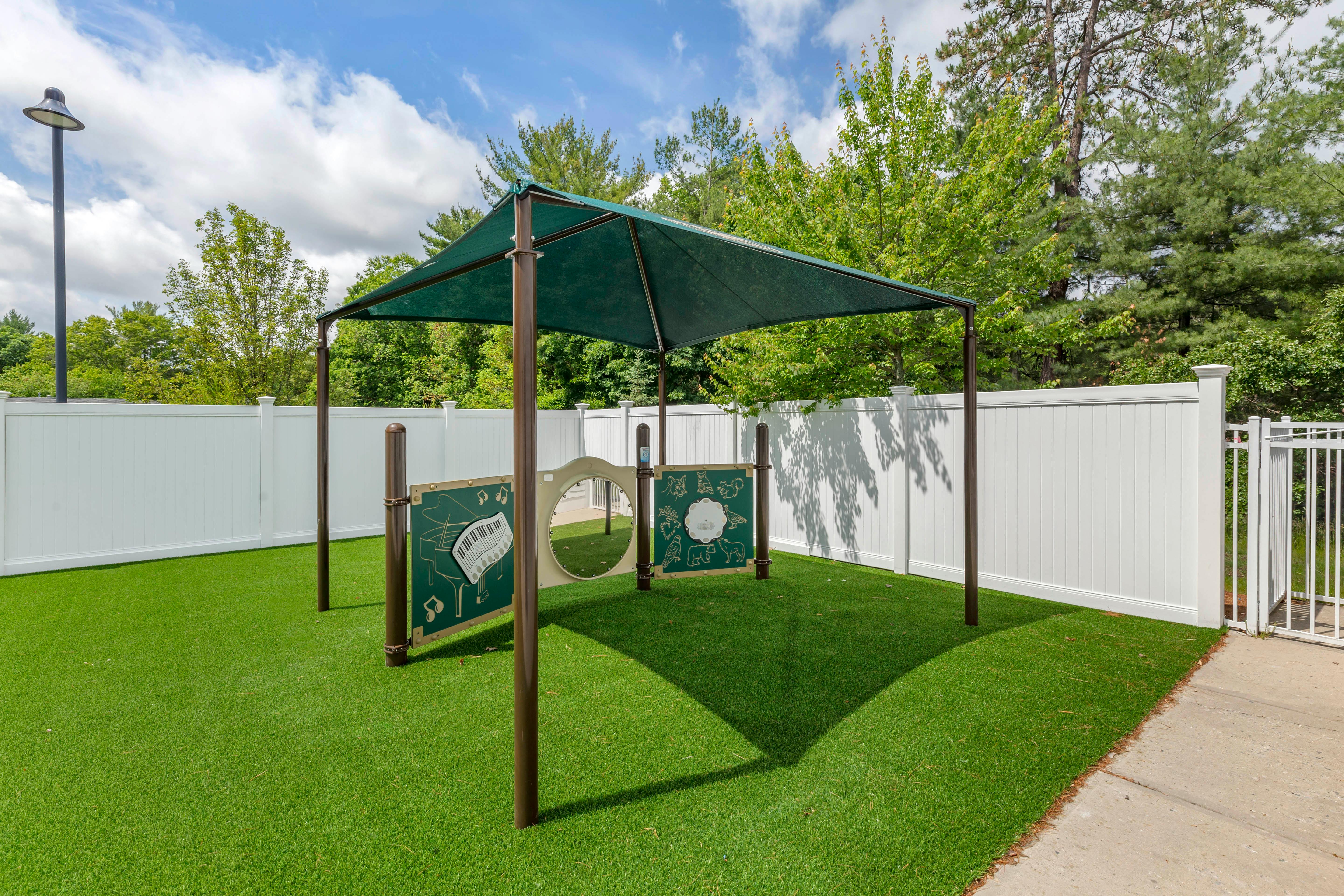 A green shaded structure covering musical play panels on artificial turf