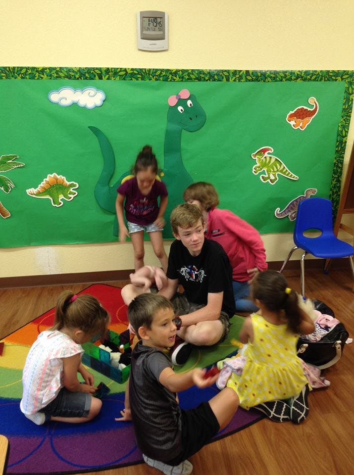 Children sitting on a colorful rug in a classroom with dinosaur decorations