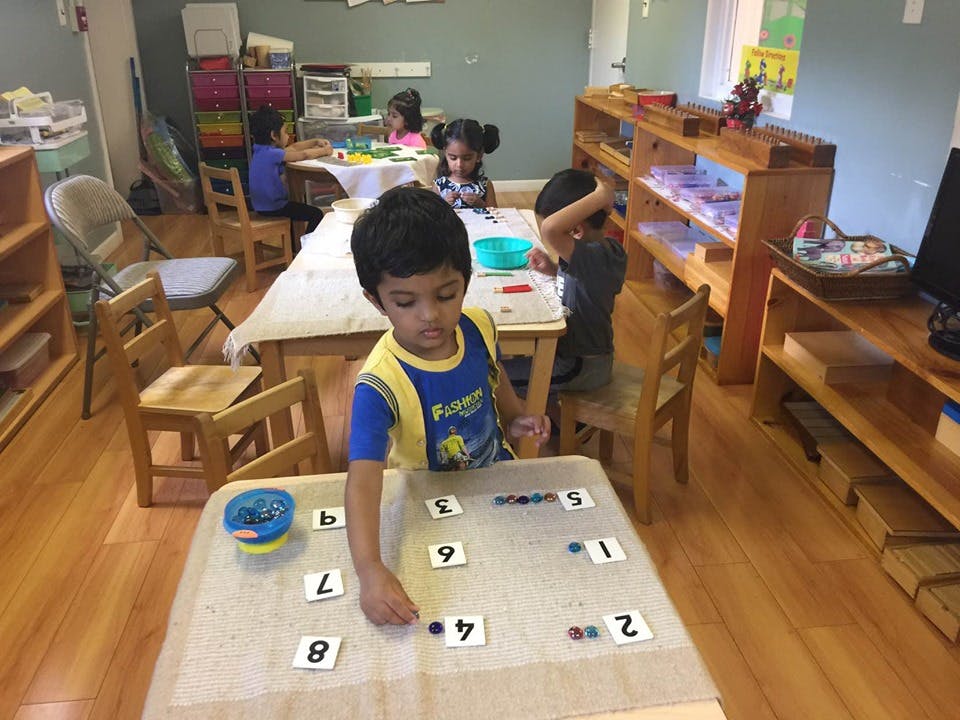 Child playing with number tiles at a table in a classroom