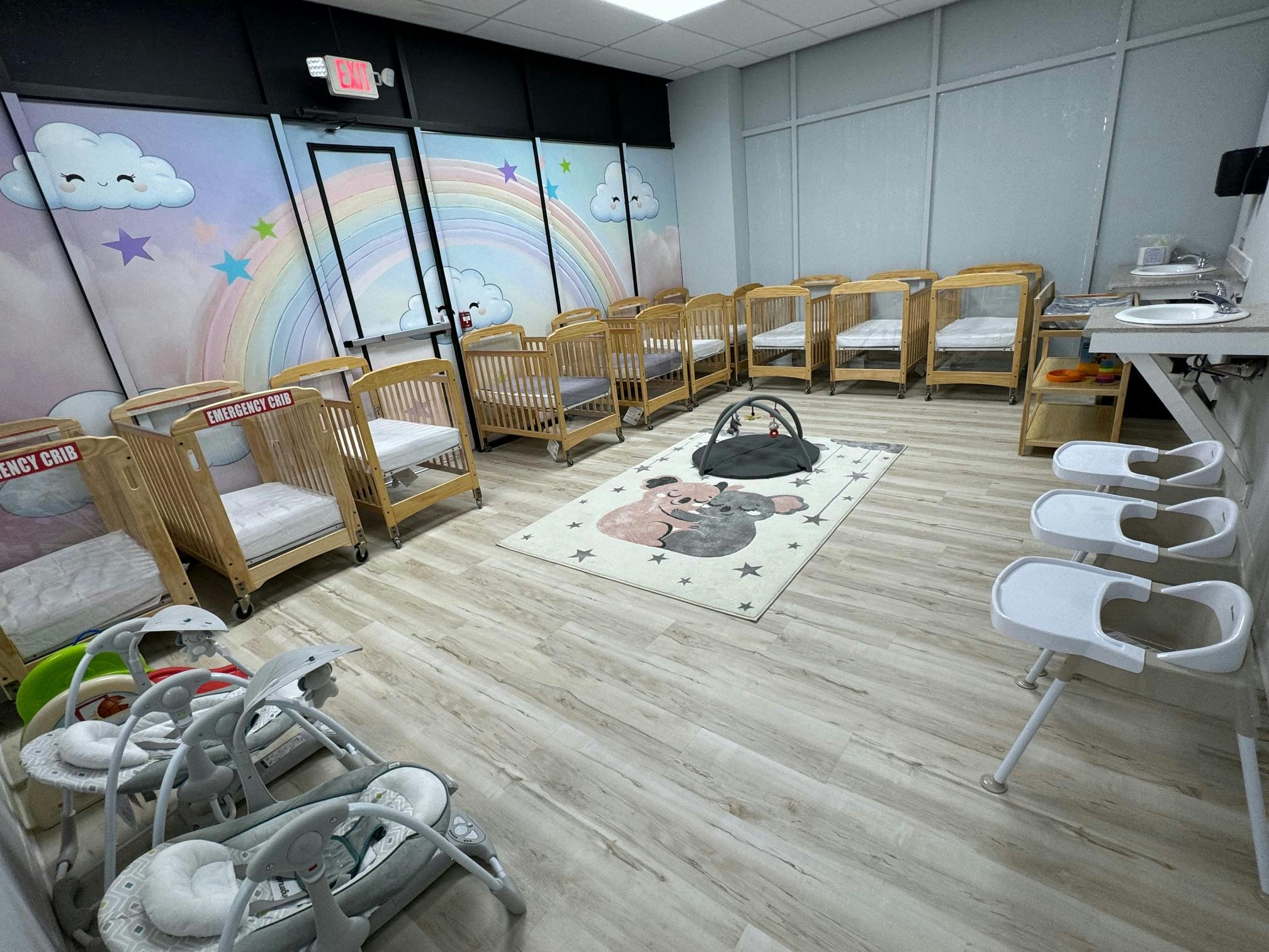 Room with multiple cribs, high chairs, and a play mat