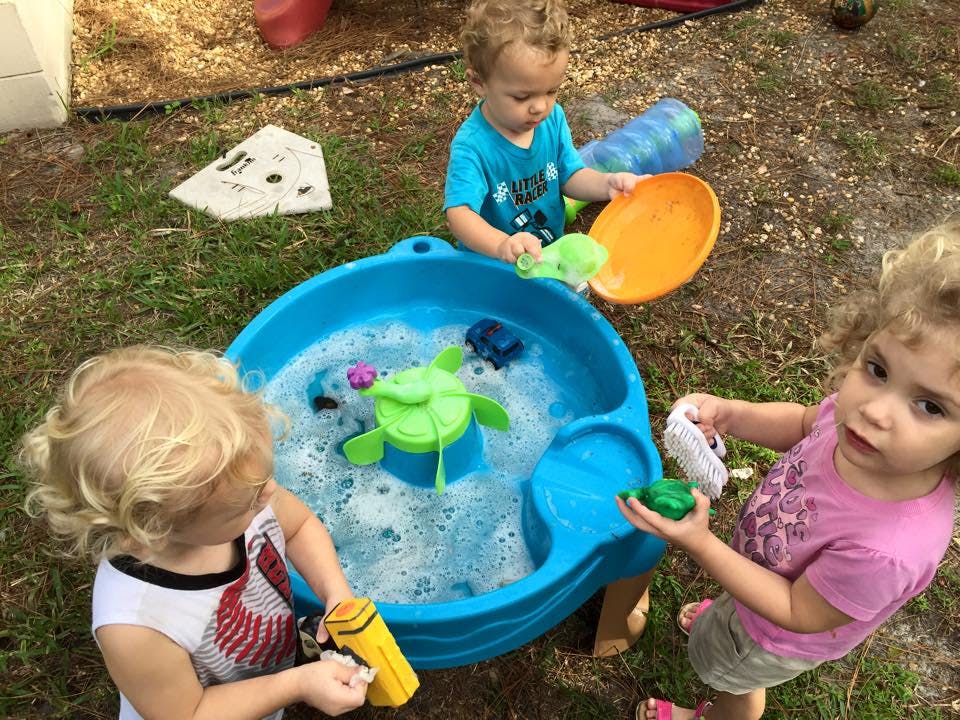 Three children playing with a water table outdoors