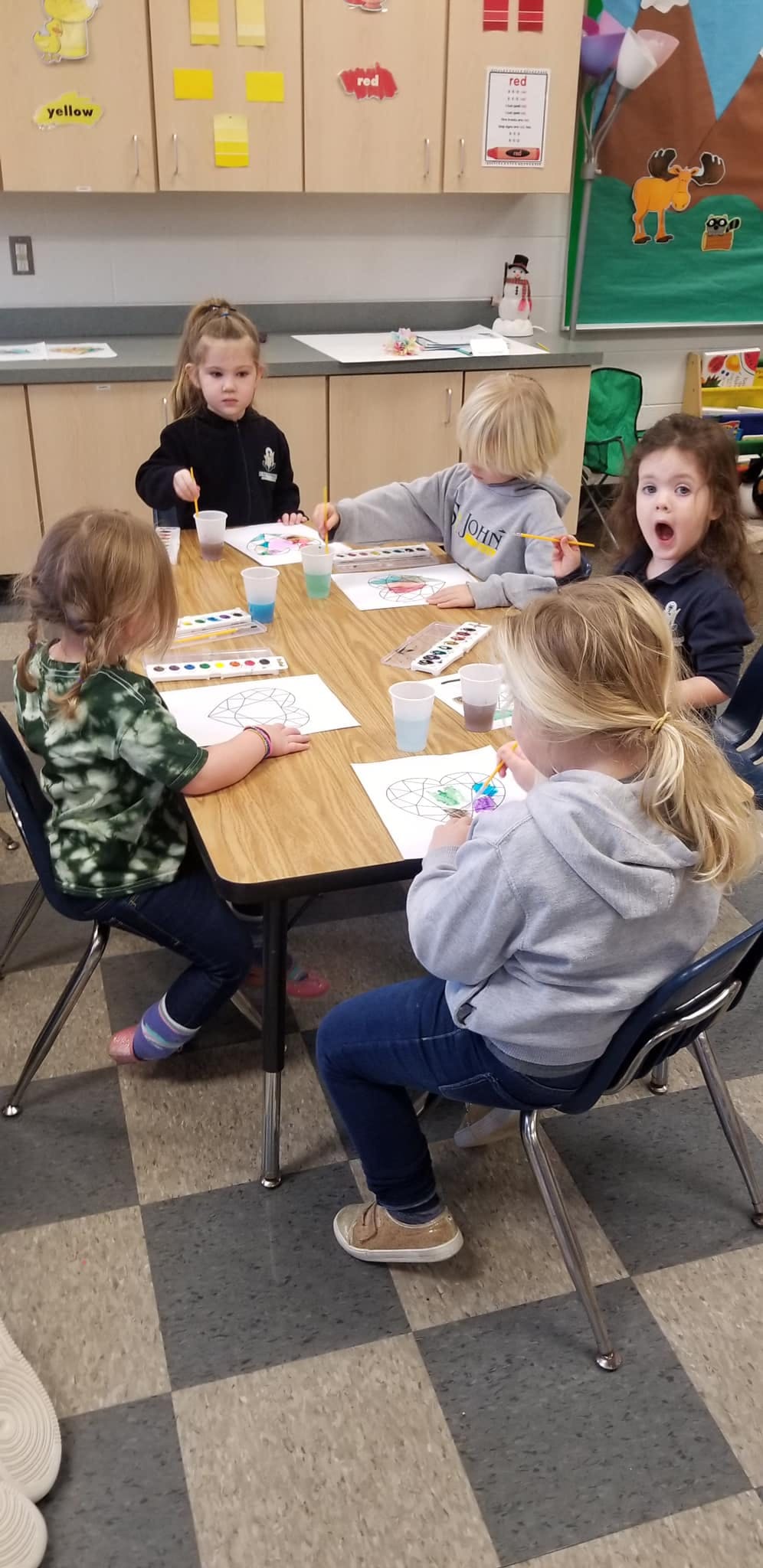 Four children painting at a table in a classroom