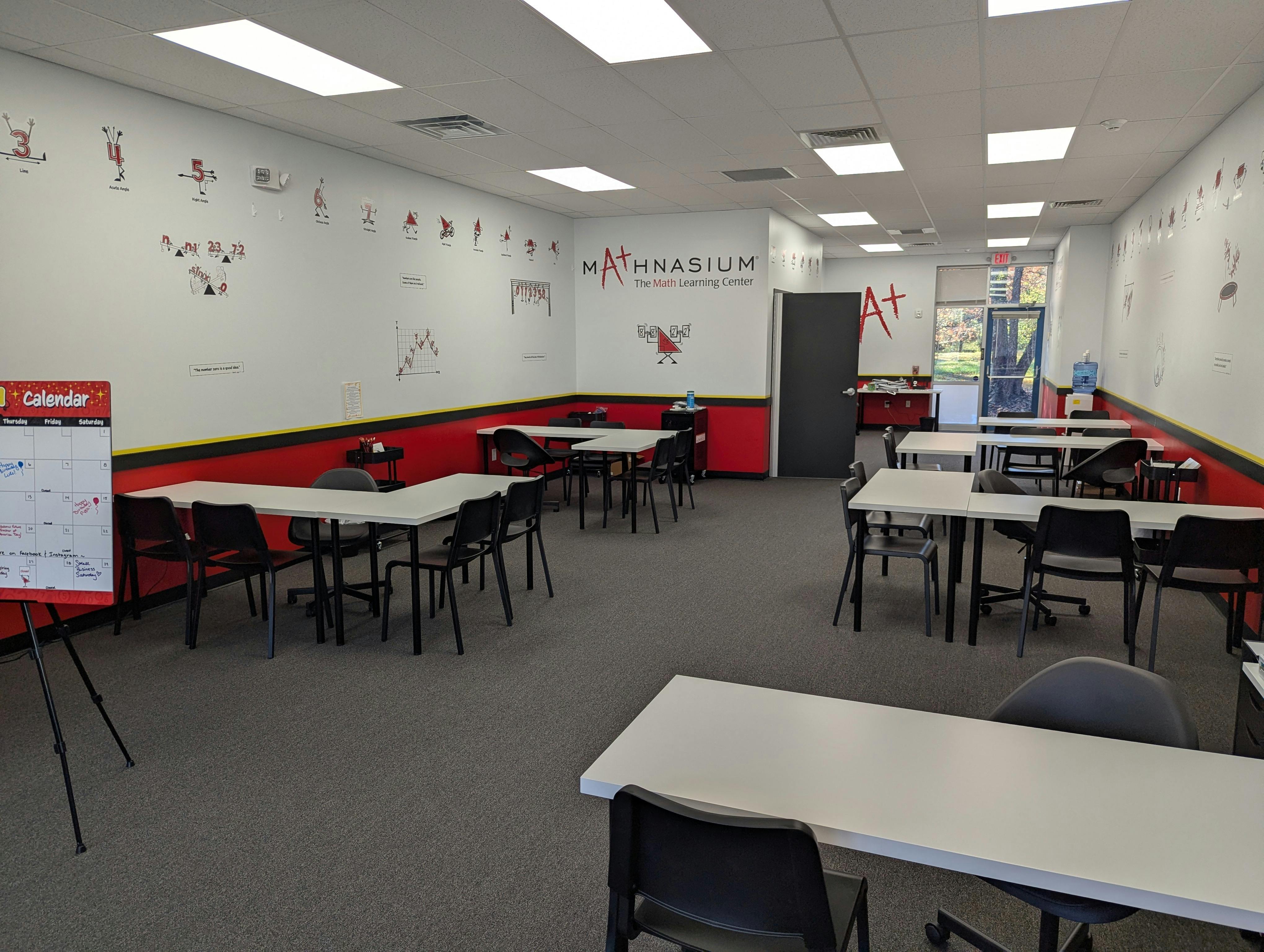 An empty learning center with white tables and black chairs, math graphics on the walls