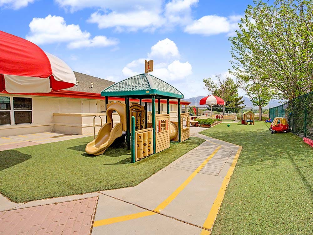 Outdoor playground with artificial turf, a slide structure, and a red and white umbrella