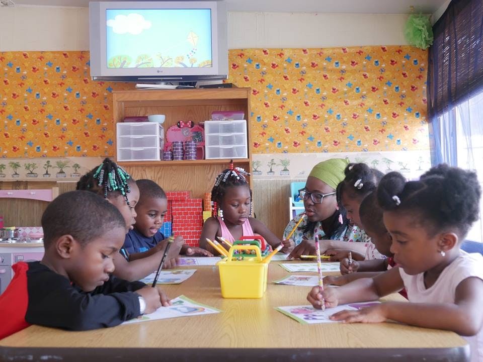 Children and an adult drawing at a table in a classroom