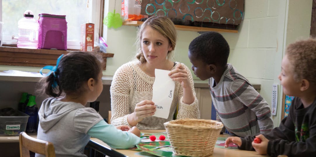 Person holding paper, surrounded by three children at a table