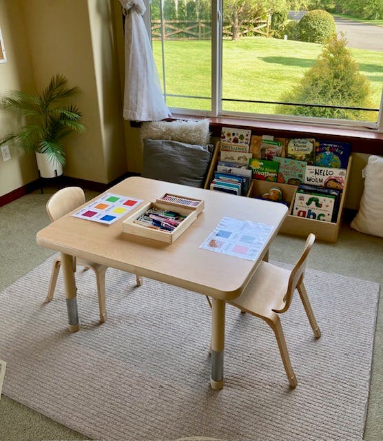 Small wooden table and chairs with art supplies and books in a room