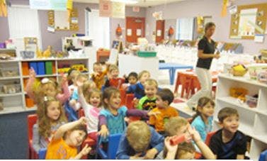 Children sitting in a classroom with an adult standing in the background