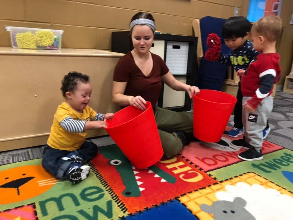 Person and three children playing with red buckets on a colorful mat