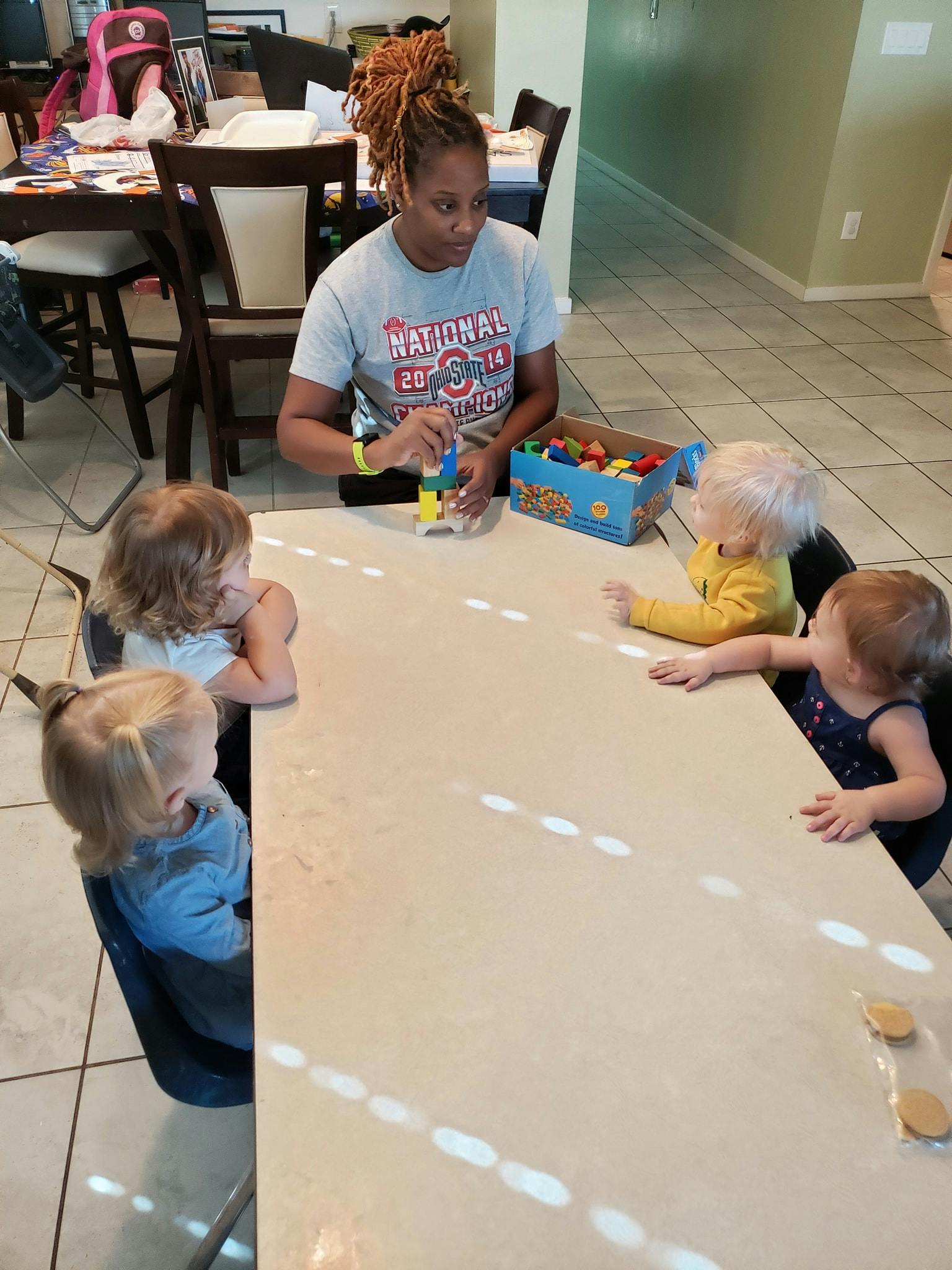 Person playing with building blocks with three children at a table