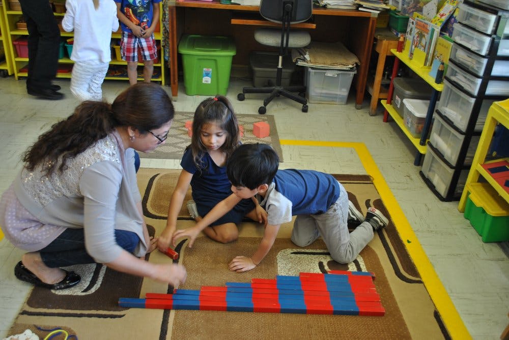 Person and two children on floor playing with red and blue blocks