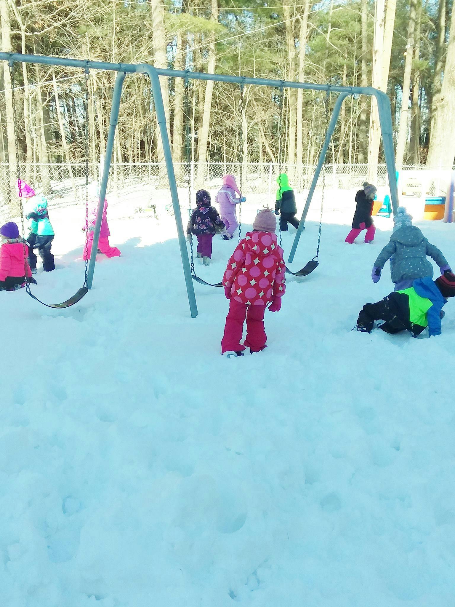 Children playing in the snow near a swing set