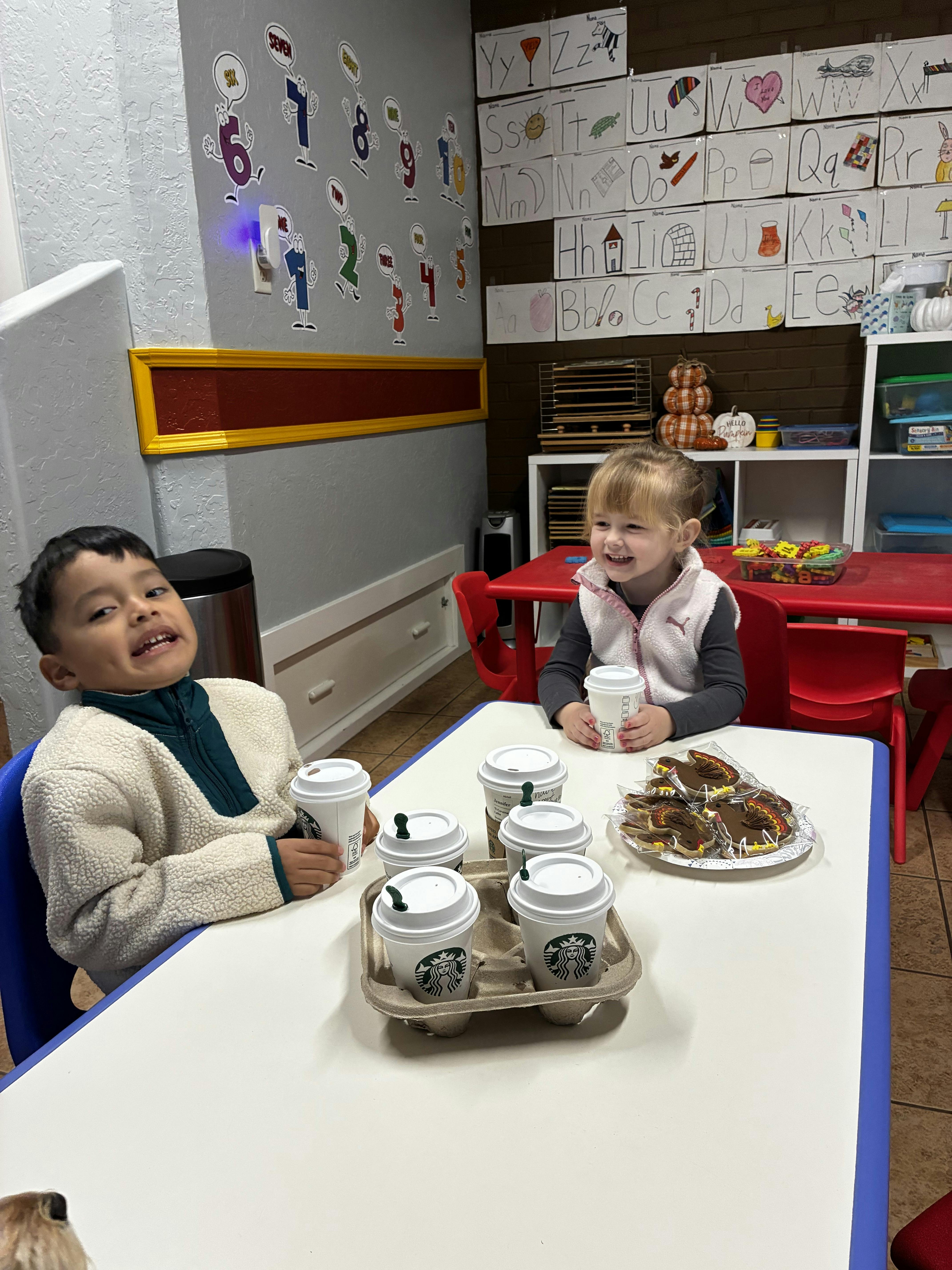 two children seated at a table with Starbucks cups and turkey-shaped cookies