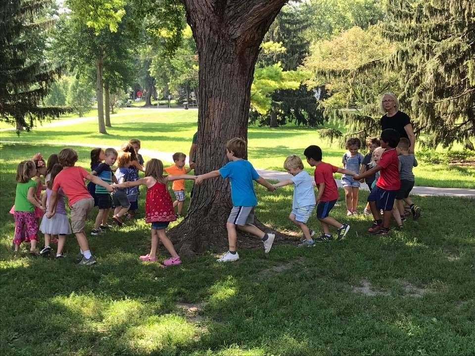 Children holding hands and walking in a circle around a tree