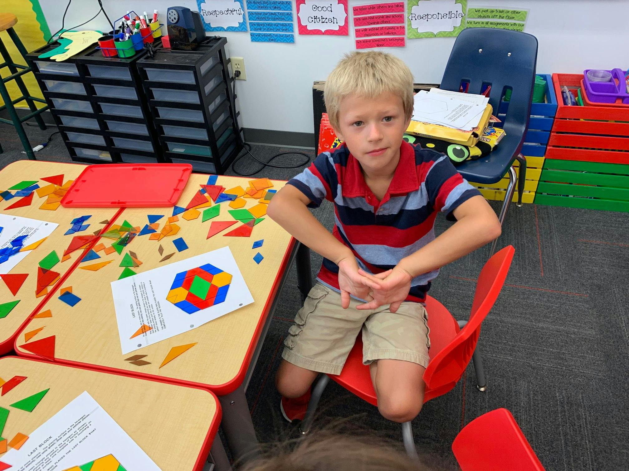 Child sitting at a table with colorful geometric shapes and a pattern sheet
