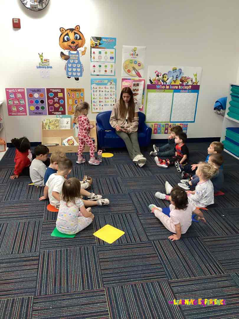 Adult sitting on a couch with children sitting on the floor in a classroom