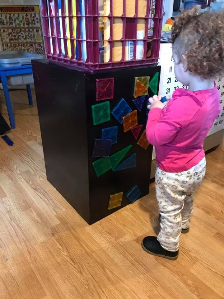 Child playing with colorful magnetic shapes on a black cabinet