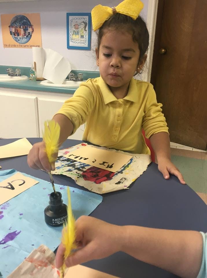 Child dipping a feather quill into an inkwell